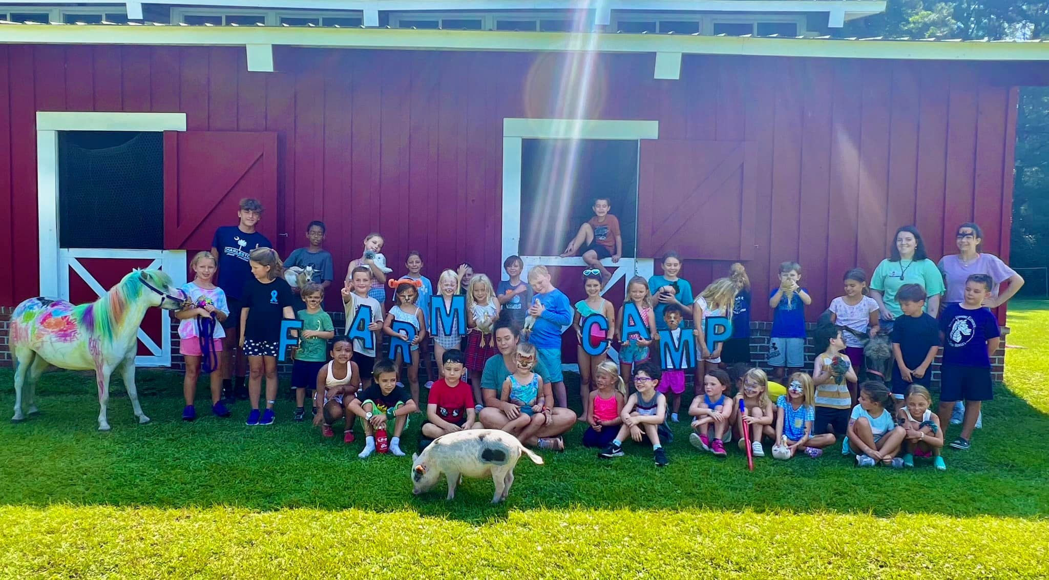 Kids at The Red Barn Farm Camp holding Farm Camp letters in front of the barn
